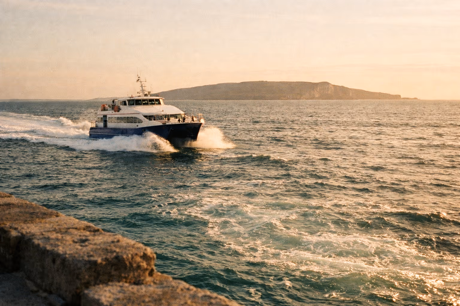 A passenger ferry travels across the sea with an island visible in the distance.