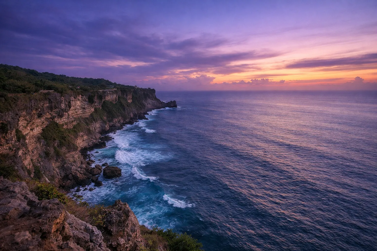Rocky cliffs of Uluwatu rise above the ocean at sunset on the coast of Bali.