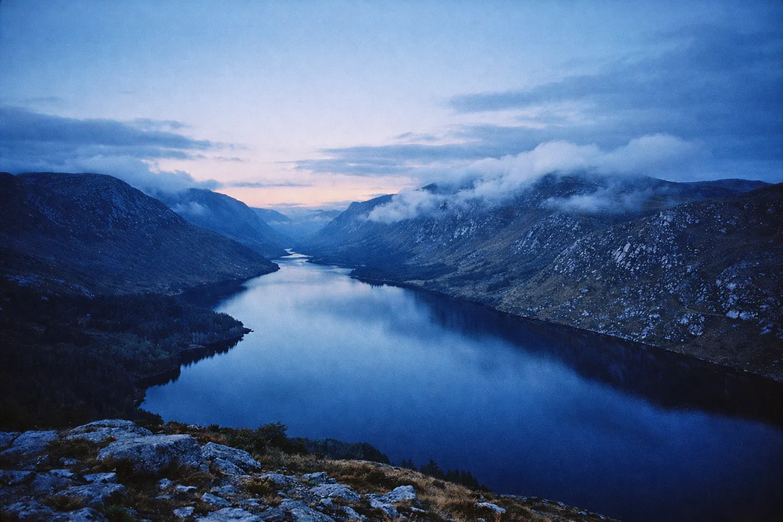 A wide lake winds between rugged mountains at dusk in Glenveagh National Park, Ireland.