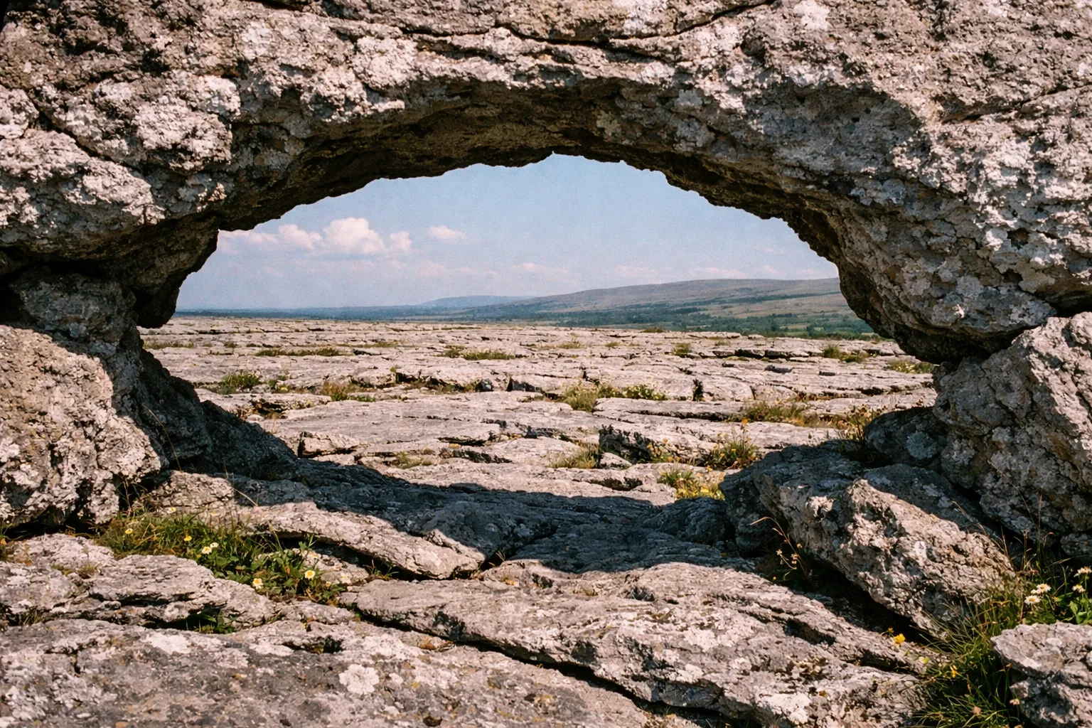 Limestone pavement and rocky arch in The Burren National Park, with distant hills under a blue sky.