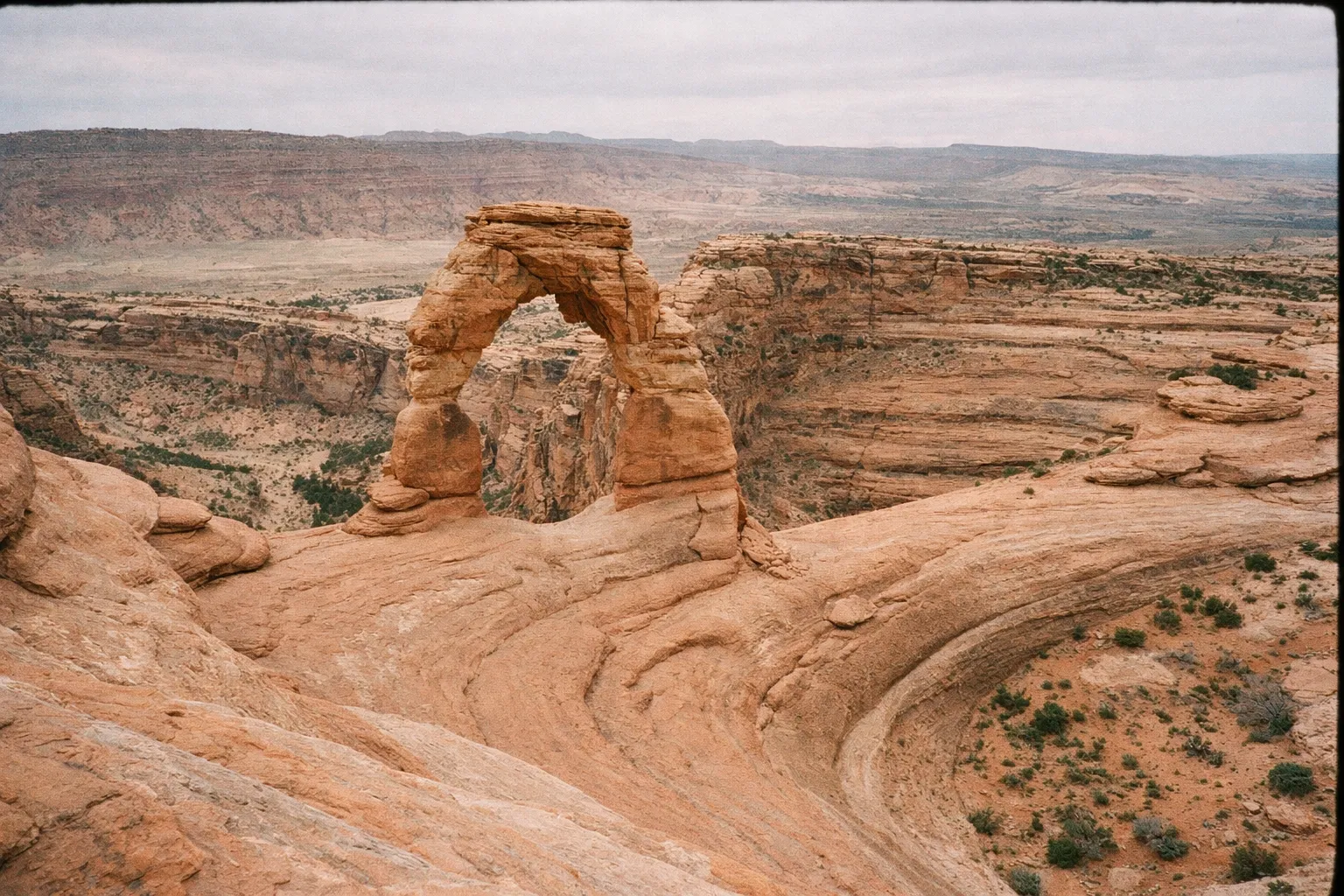 Delicate Arch stands on a rocky plateau with canyons and mesas in Arches National Park, Utah.