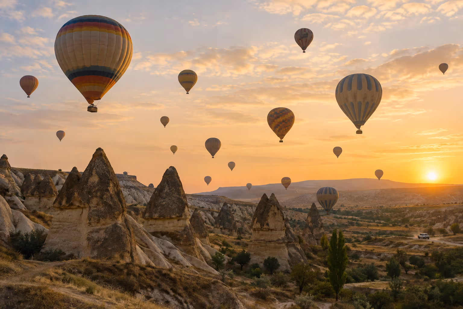 Hot air balloons rise over Cappadocia's rock formations at sunrise.