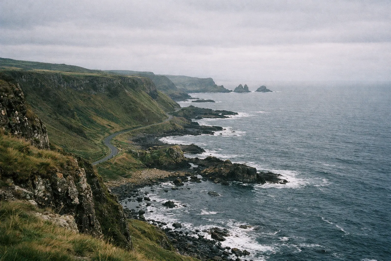 A winding coastal road runs along steep cliffs above the sea on Northern Ireland's Causeway Coastal Route.