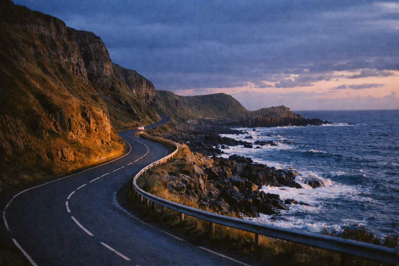 A winding road runs along rocky cliffs beside the sea at Giant's Causeway on the Causeway Coastal Route.