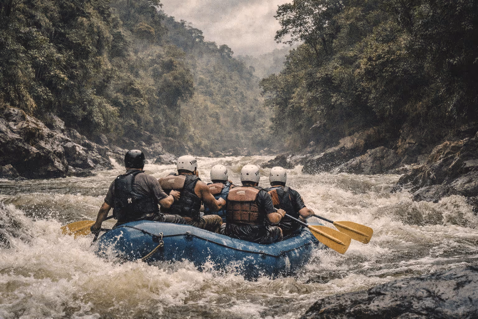 A group of people whitewater rafting on a river surrounded by dense jungle and rocky cliffs.