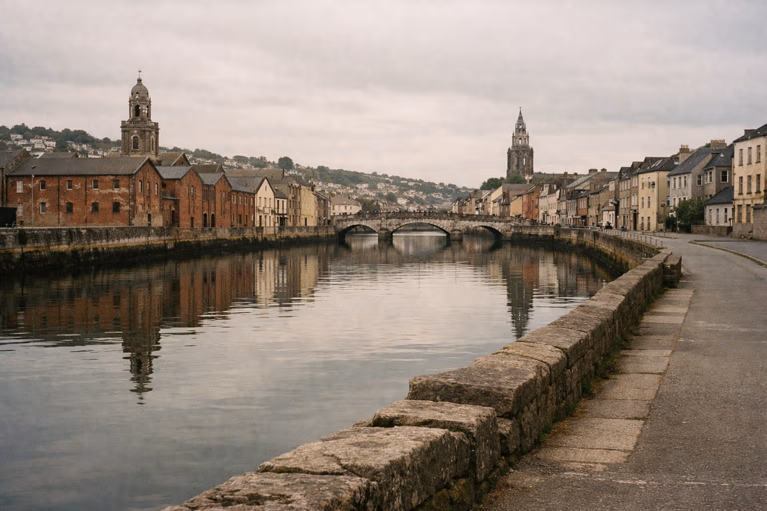 A calm river runs through the center of Cork, Ireland, lined with historic buildings and crossed by a stone bridge.