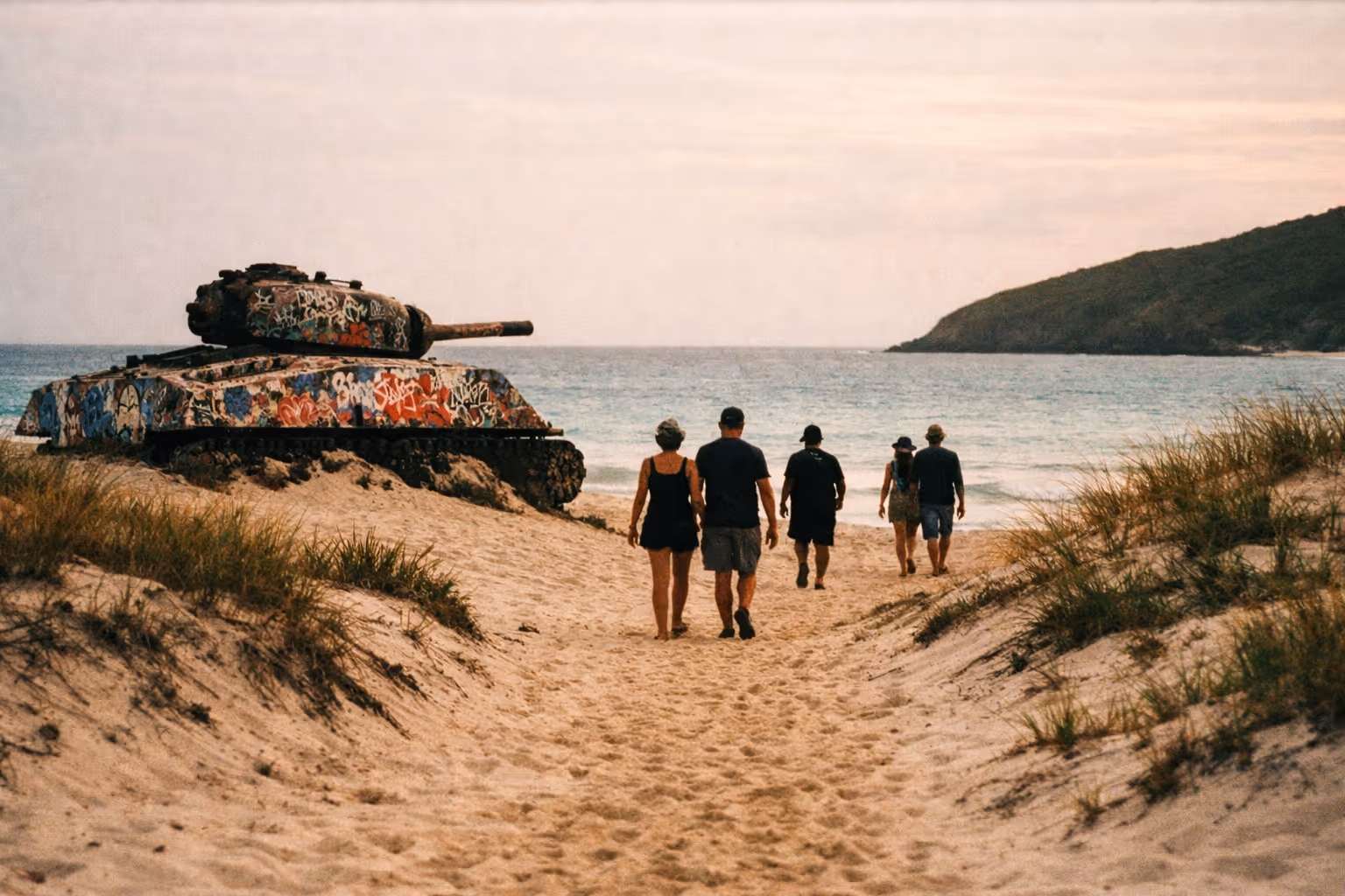 People walk on sandy Flamenco Beach past a graffiti-covered tank toward the ocean in Culebra, Puerto Rico.
