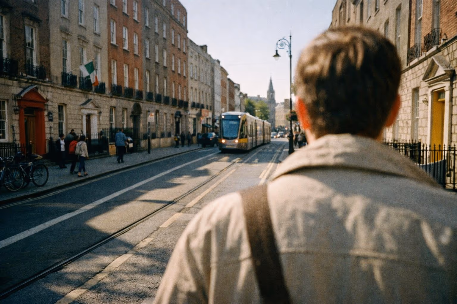 People walk along a busy Dublin street lined with shops and view of a church in the distance.