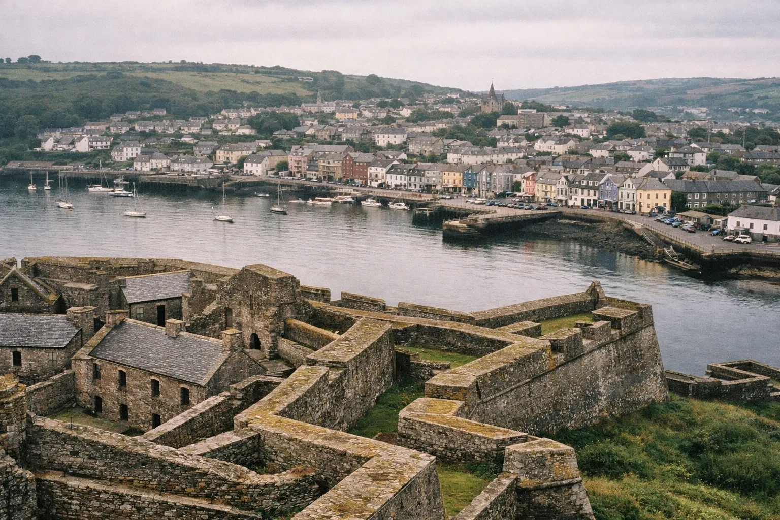 A stone fort overlooks a harbor lined with colorful buildings in a seaside town.