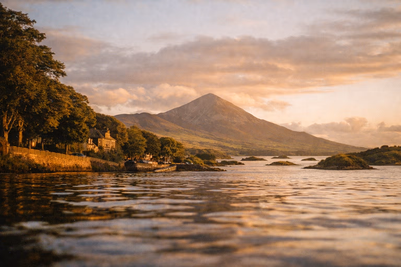 Croagh Patrick mountain rises behind the harbor and waterfront homes in Westport, Ireland at sunset.