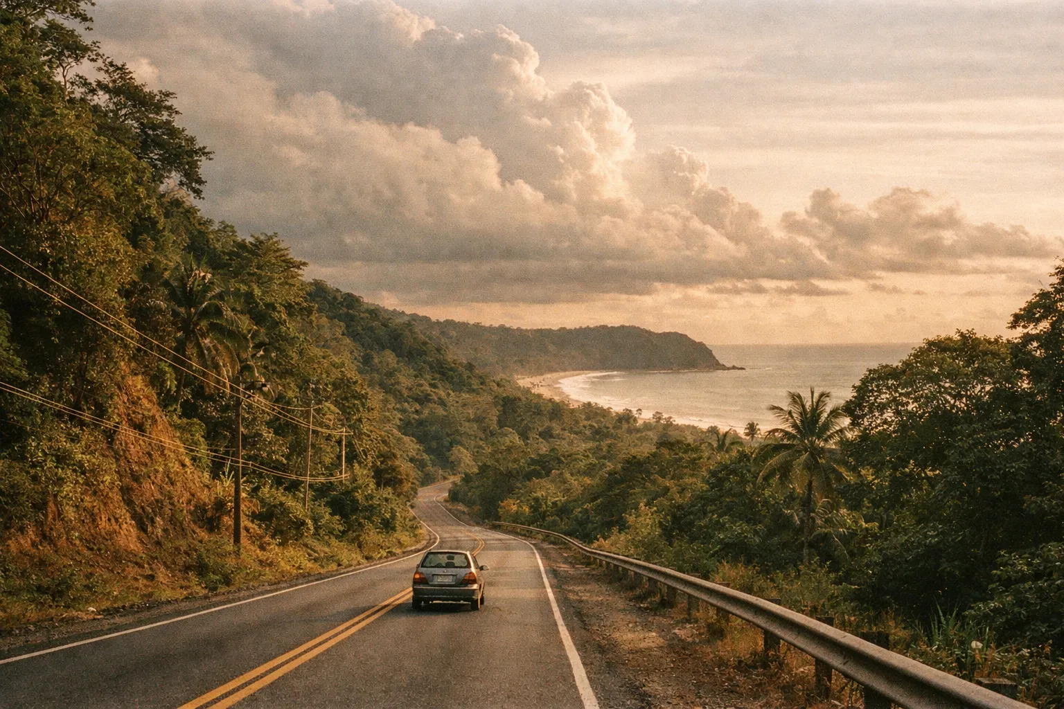 Sunlit Costa Rican highway winding through tropical forest toward a distant beach, with a small car on the road at golden hour.