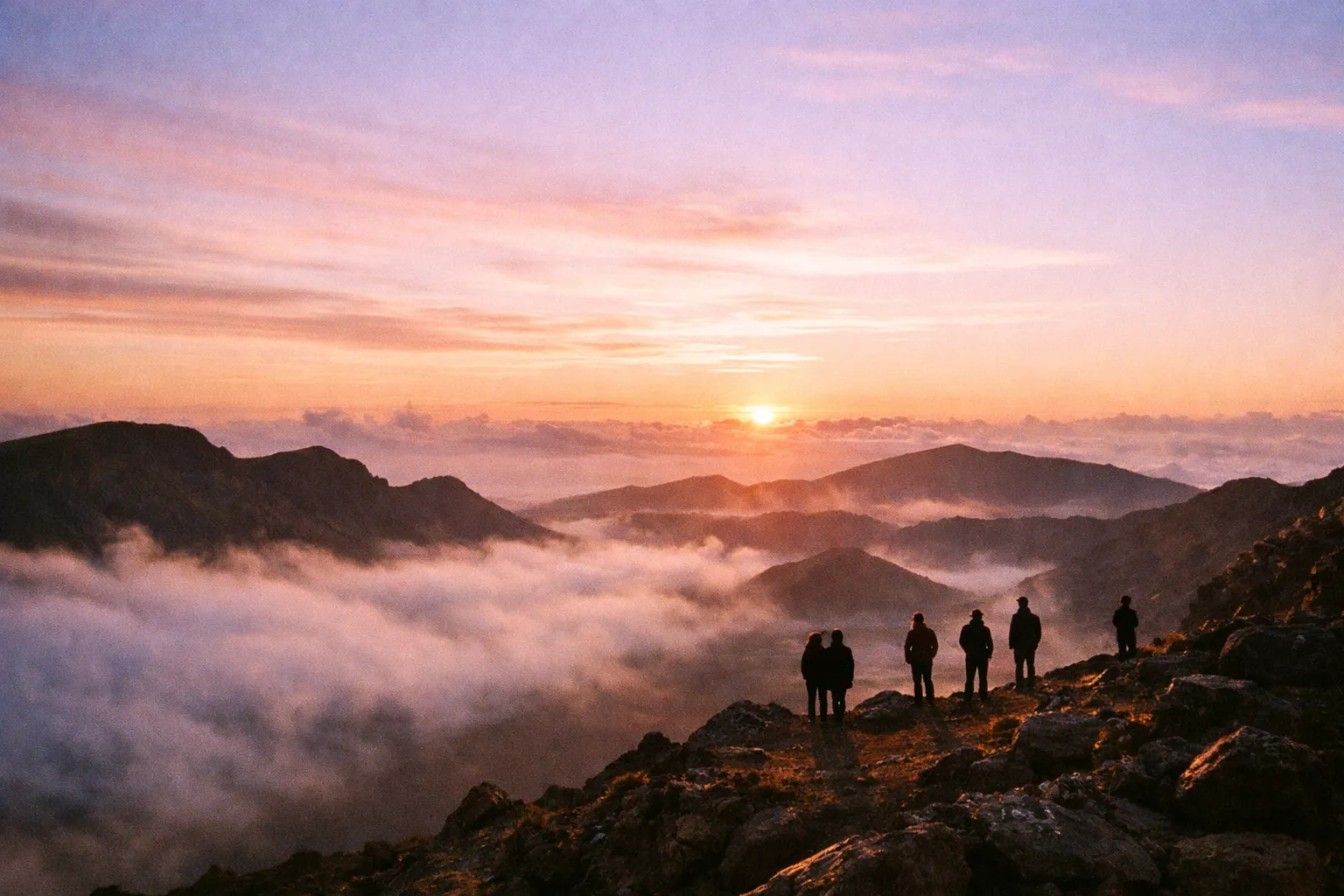 Silhouetted figures at Haleakalā summit during sunrise with crater rim and pastel sky