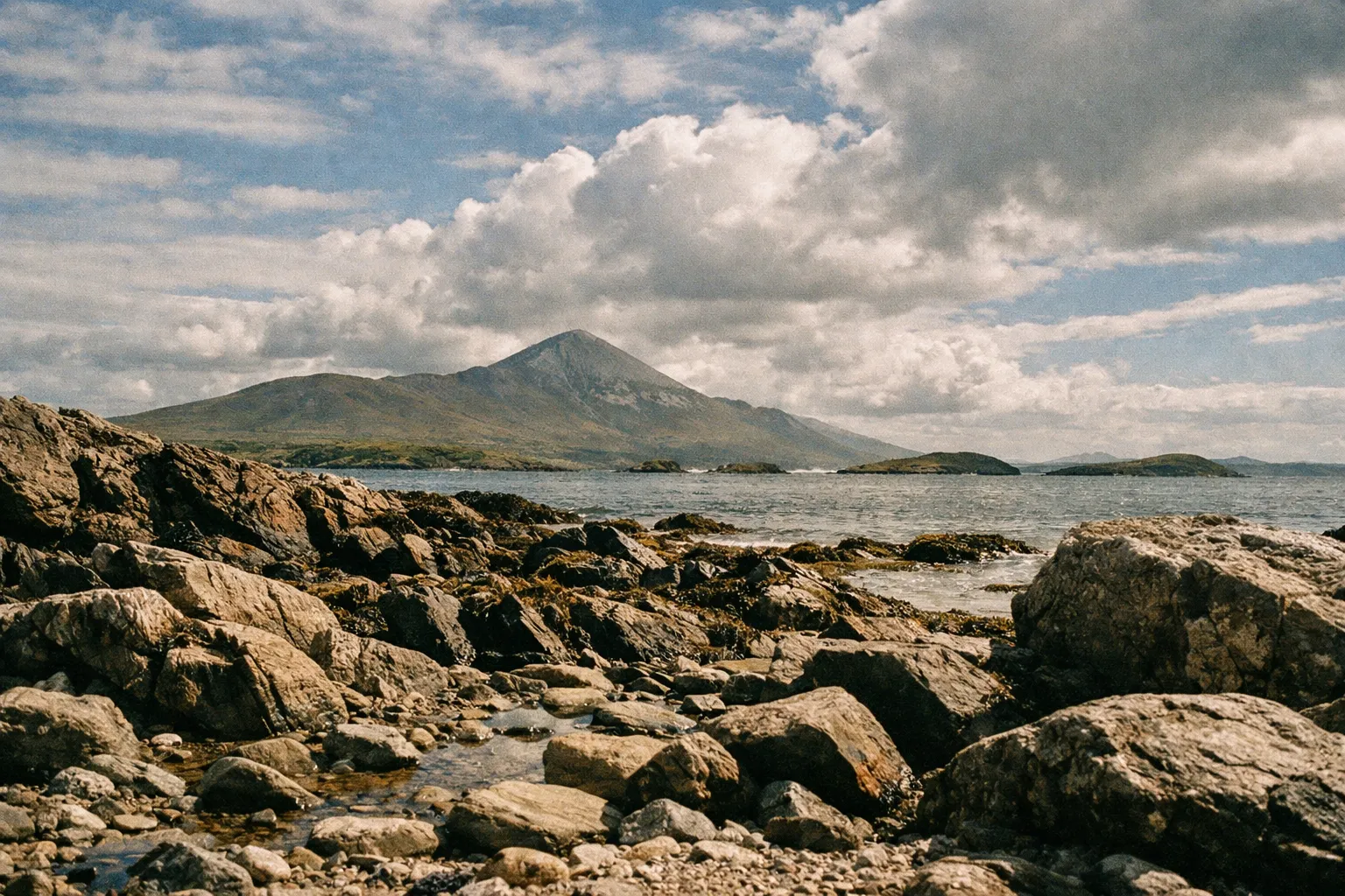 Croagh Patrick mountain rises above the rocky shoreline and water under a partly cloudy sky in County Mayo, Ireland.