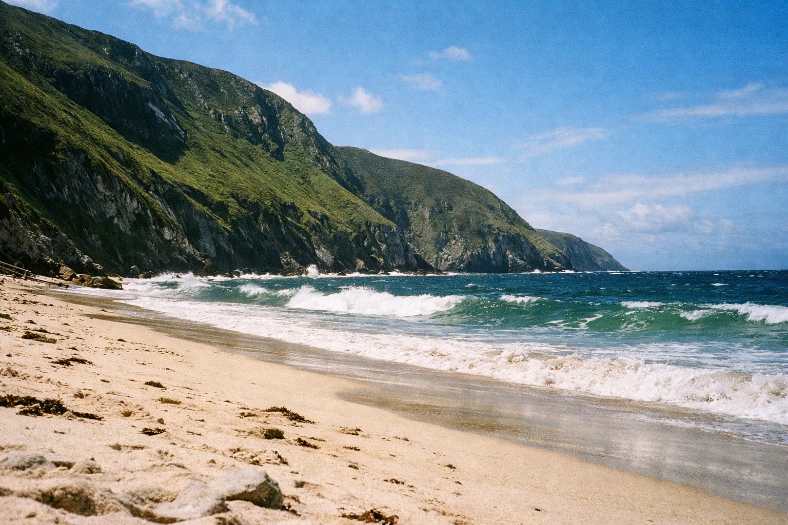Golden sand beach with waves and steep green cliffs on Achill Island along the Wild Atlantic Way, County Mayo.