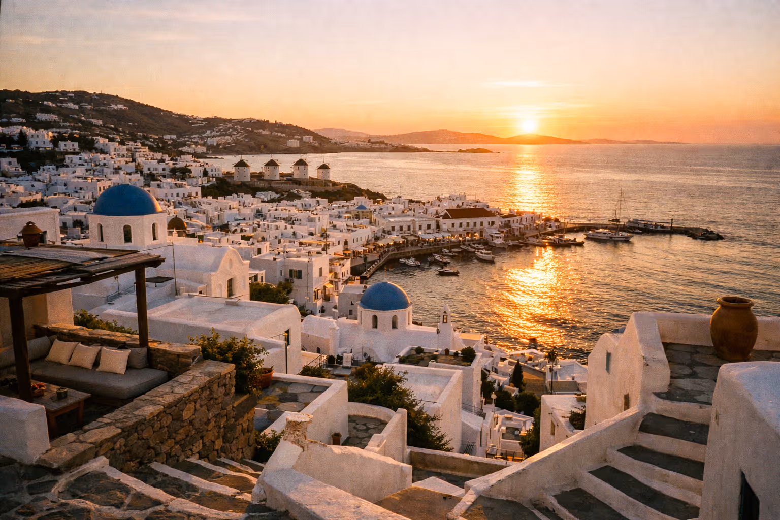Panoramic aerial view of Mykonos at sunset with white houses cascading toward the Aegean