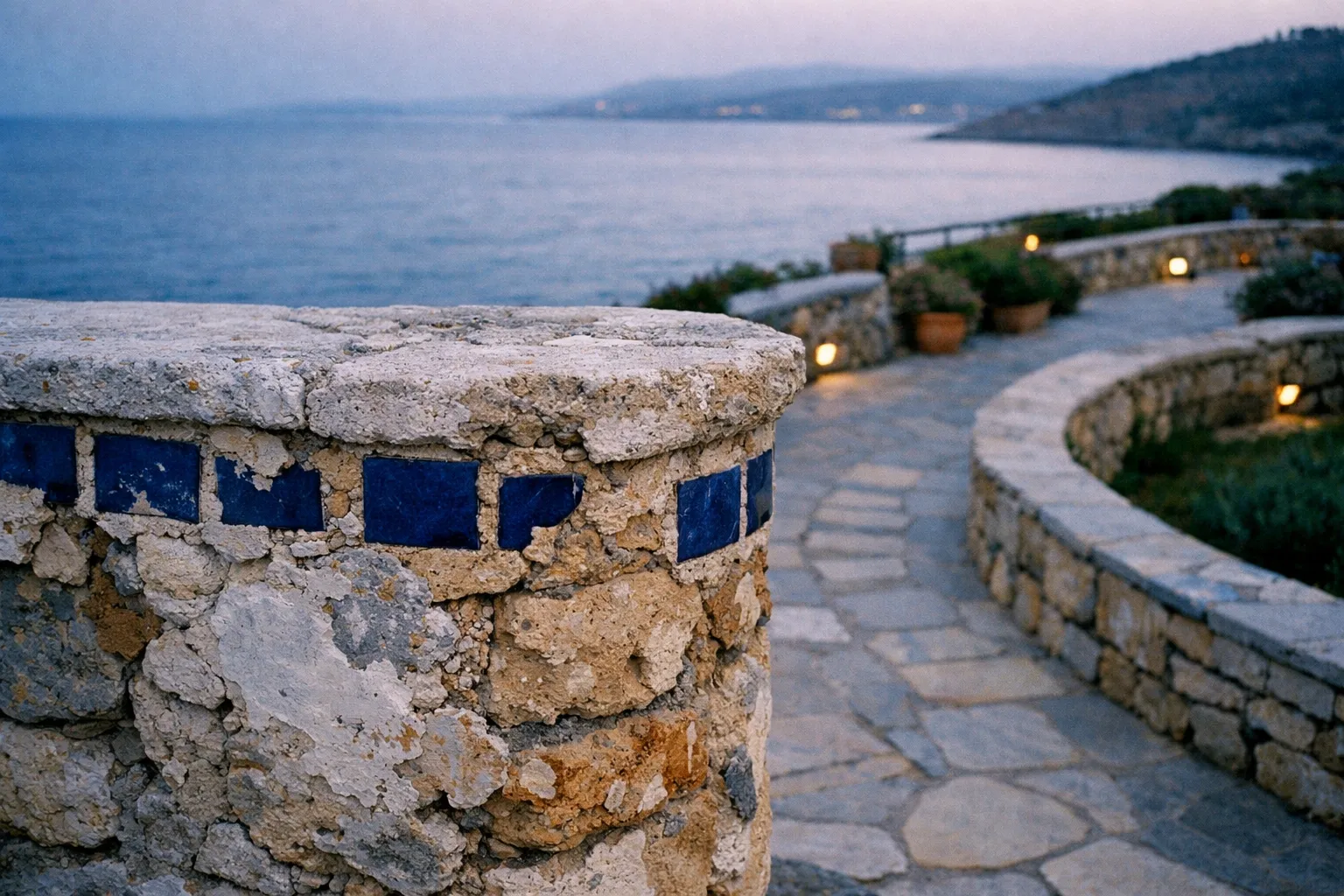 Stone walkway with curved stone wall and blue tile accents overlooking the sea at dusk