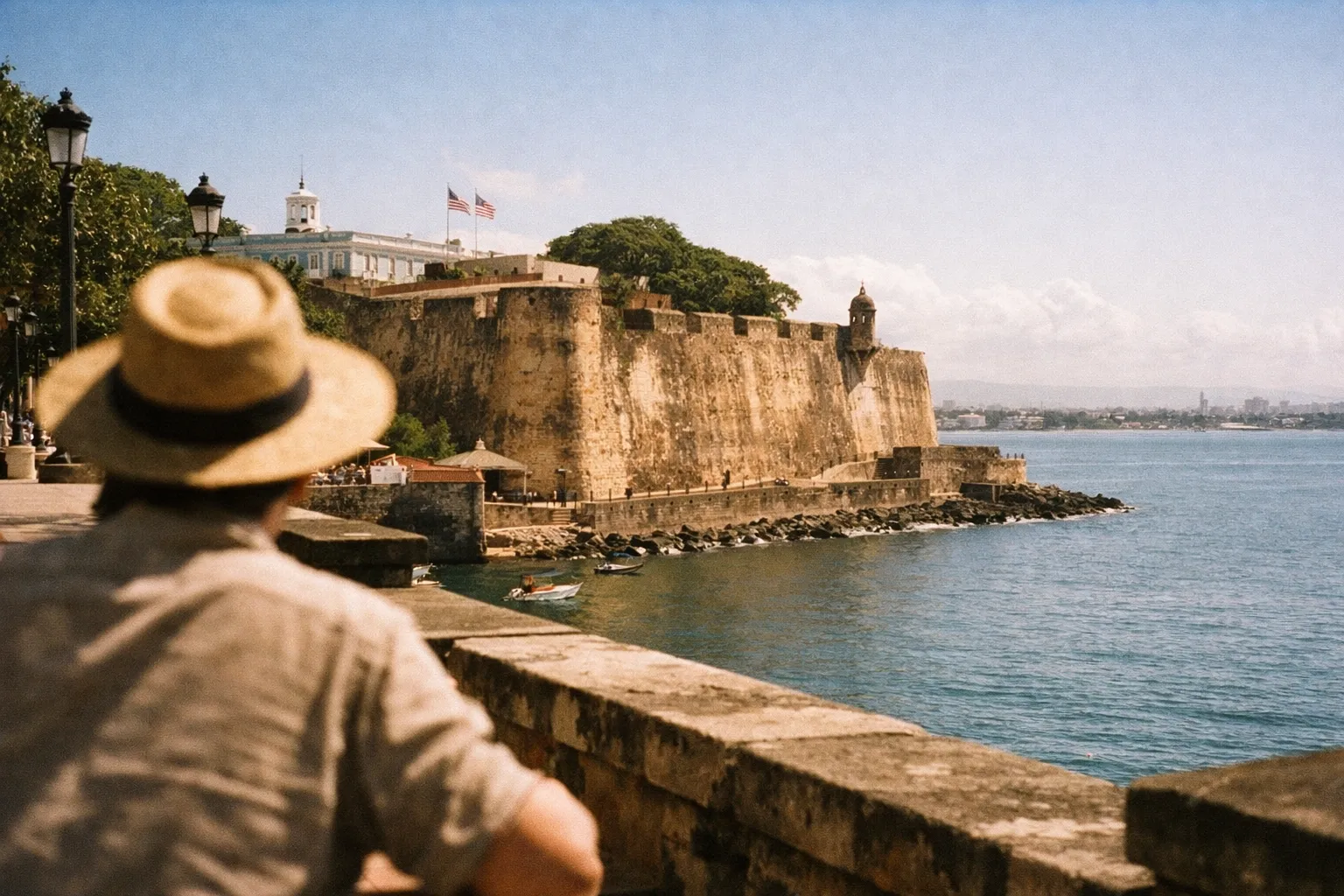 A person in a straw hat looks toward the historic stone fort of Castillo San Felipe del Morro by the San Juan waterfront.