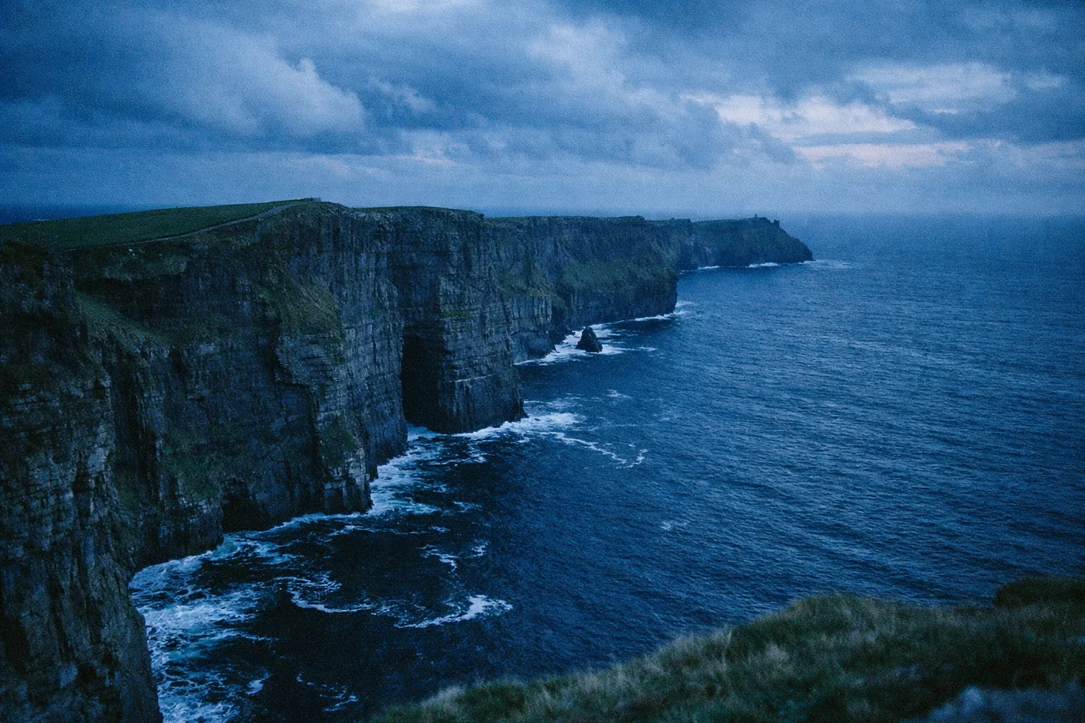 The Cliffs of Moher rise above the Atlantic Ocean under a cloudy sky in western Ireland.