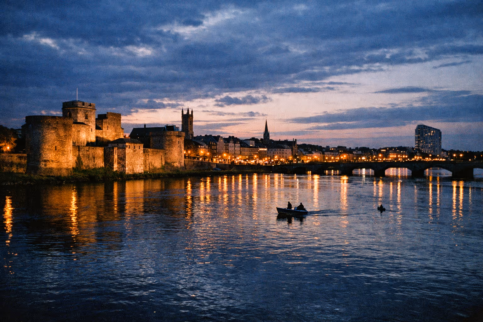 King John's Castle and the city of Limerick along the River Shannon at dusk with a small boat in the water.