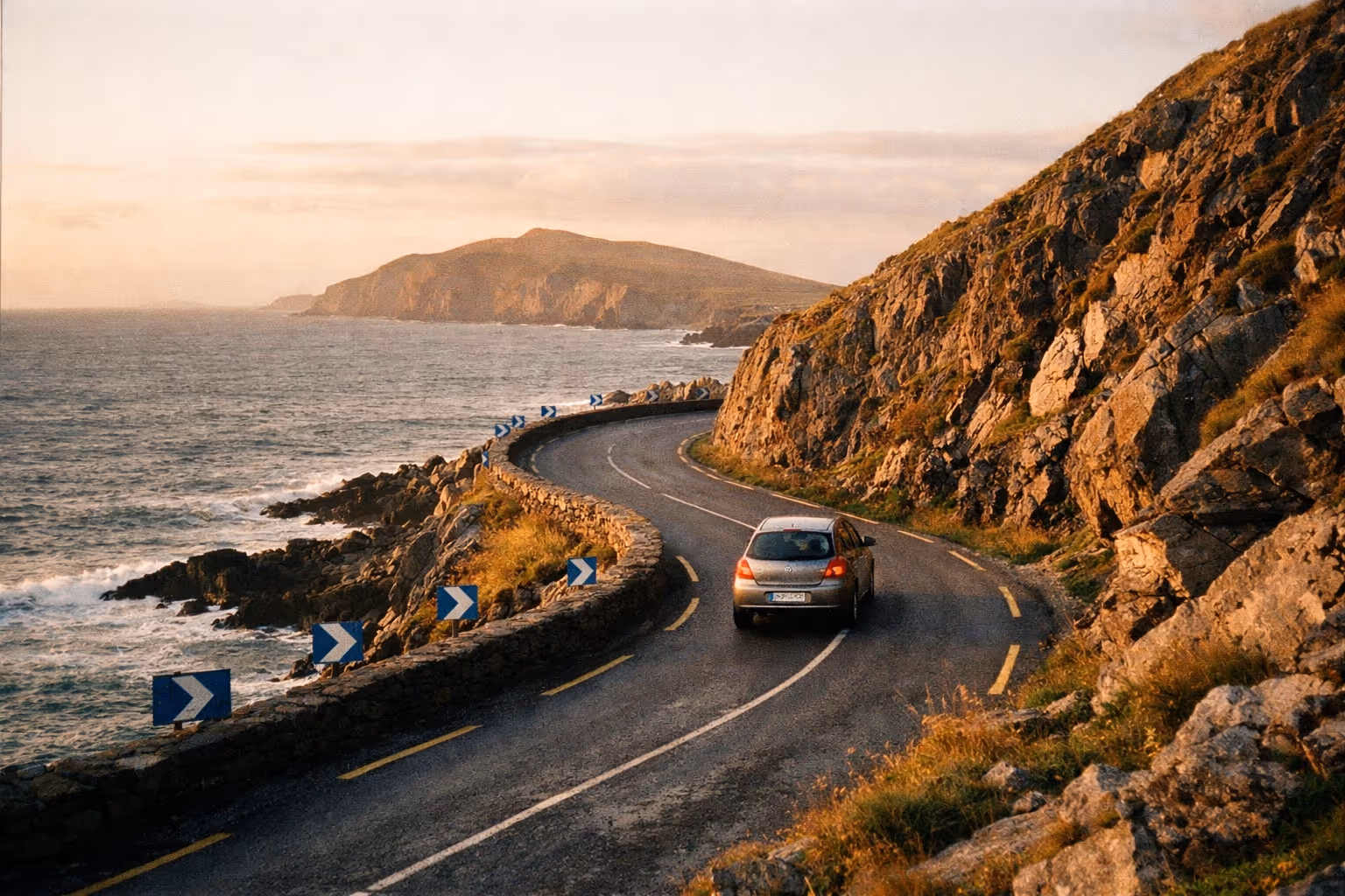 A car drives along a winding coastal road with cliffs and the ocean on the Wild Atlantic Way in Ireland.