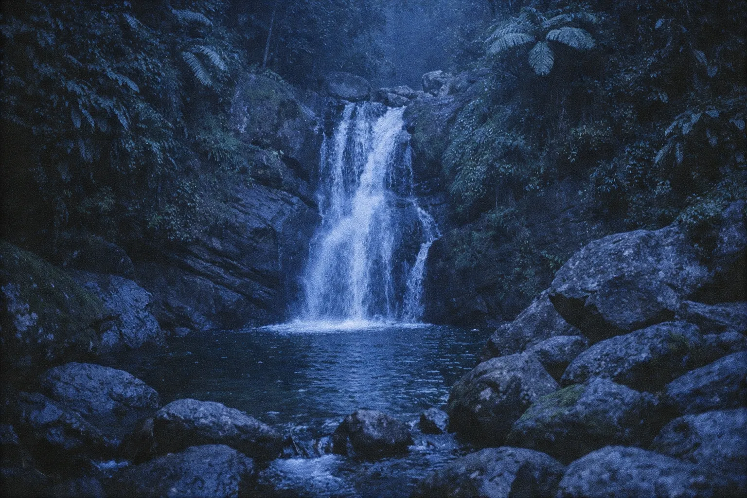 A waterfall cascades into a rocky pool surrounded by lush rainforest in El Yunque National Forest.