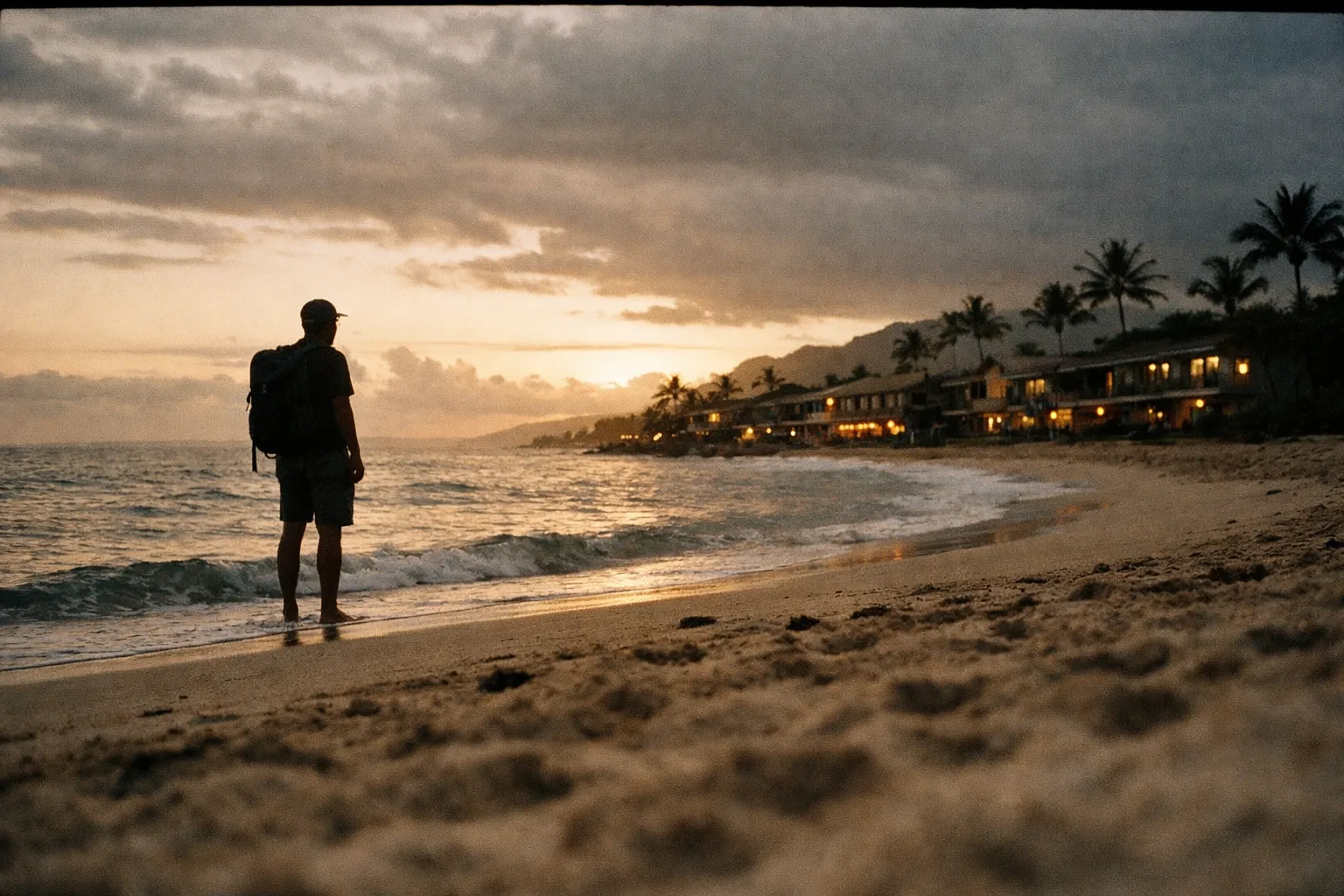 Silhouette of a traveler with a backpack on a Hawaiian beach at golden hour with budget hostels along the coast