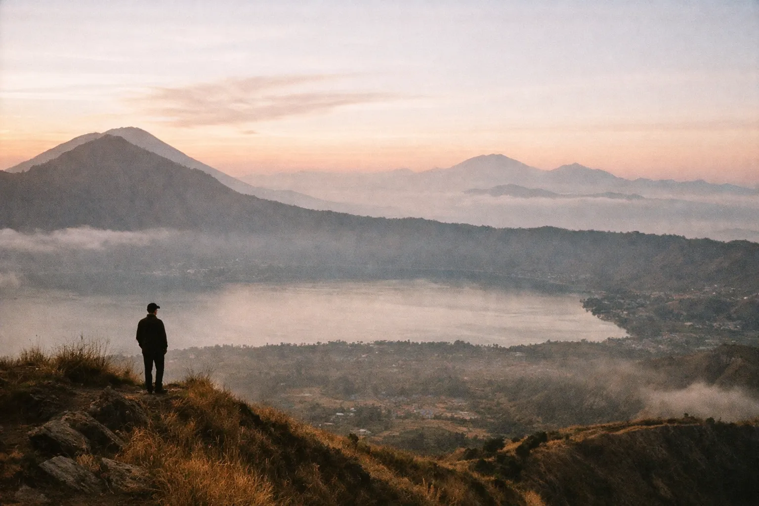 Dawn caldera view with Lake Batur and a distant hiker silhouette on the rim