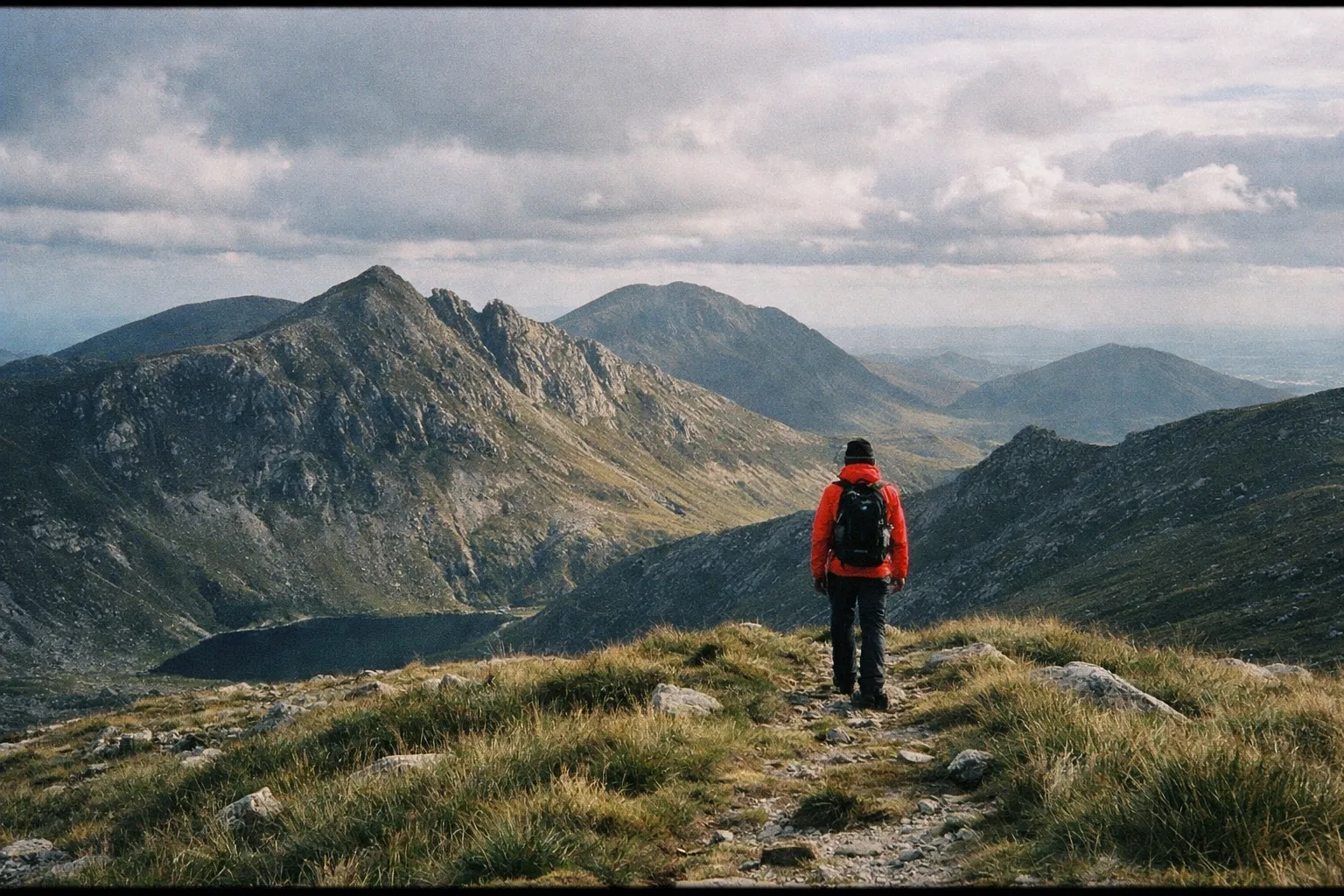 A hiker in a red jacket walks along a mountain trail overlooking the Mourne Mountains in Northern Ireland.