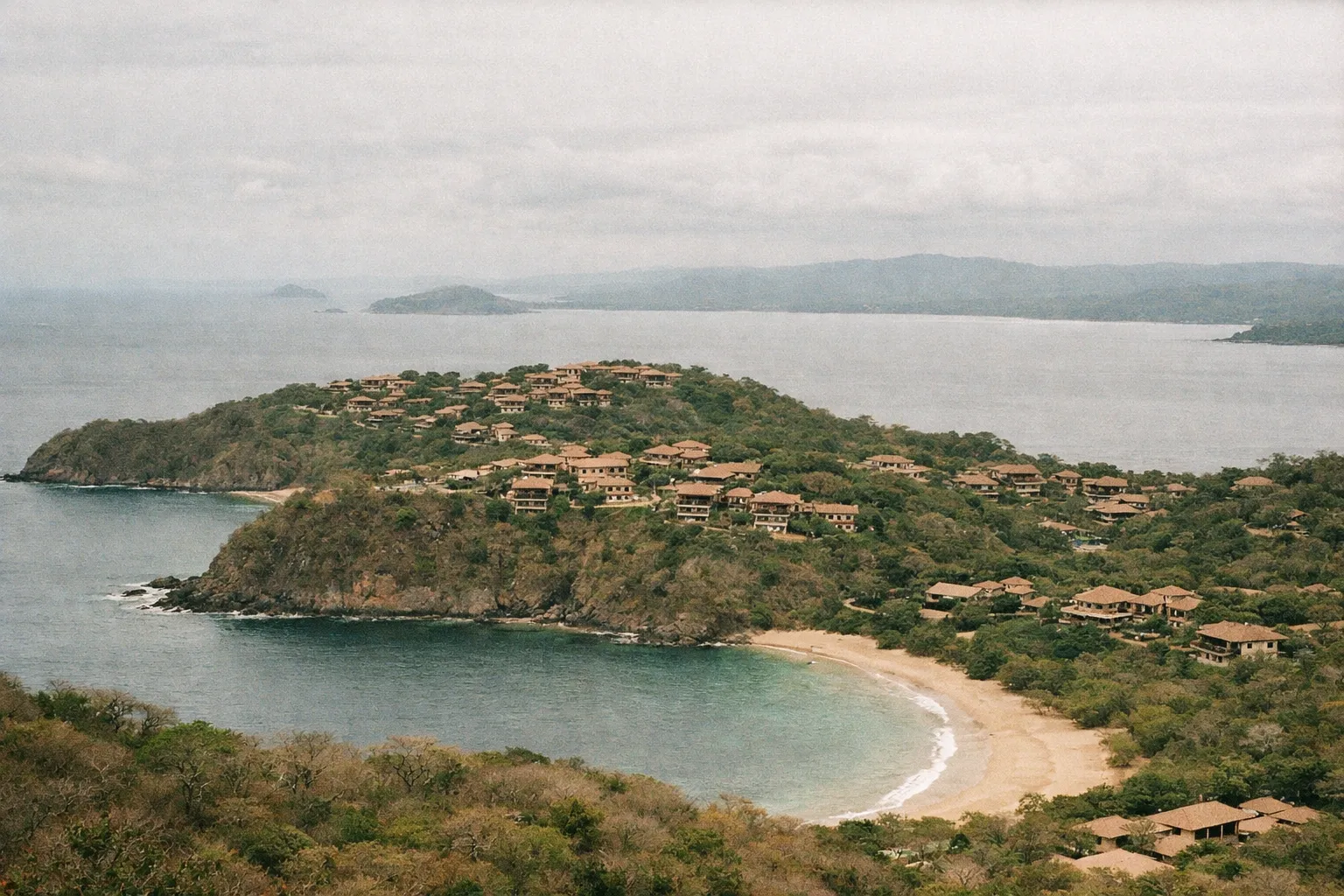 Resort villas on a green peninsula above a curved beach and the ocean at Peninsula Papagayo, Costa Rica.