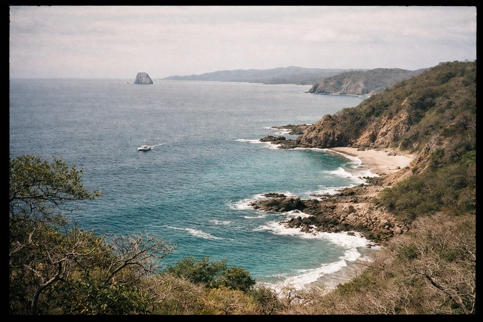 A boat cruises near the rocky coastline and secluded beaches of Peninsula Papagayo, Costa Rica.
