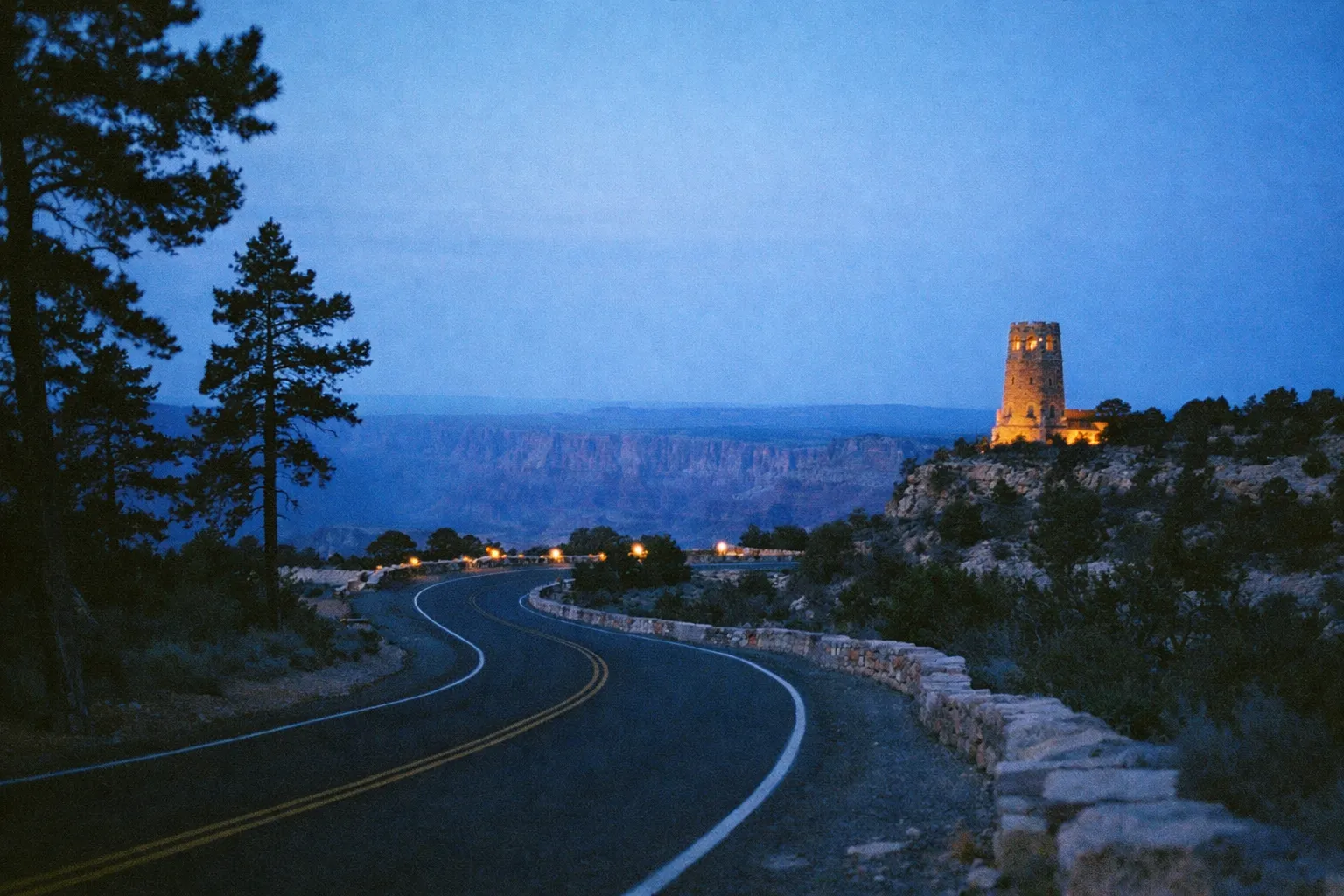 Desert View Watchtower at dusk overlooking the Grand Canyon with a winding road in the foreground.