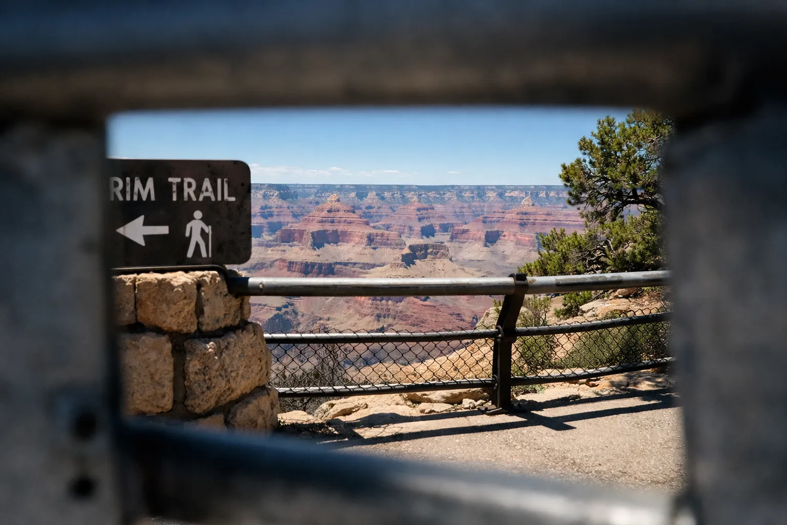 View of Grand Canyon and Rim Trail sign seen through a railing at an overlook.