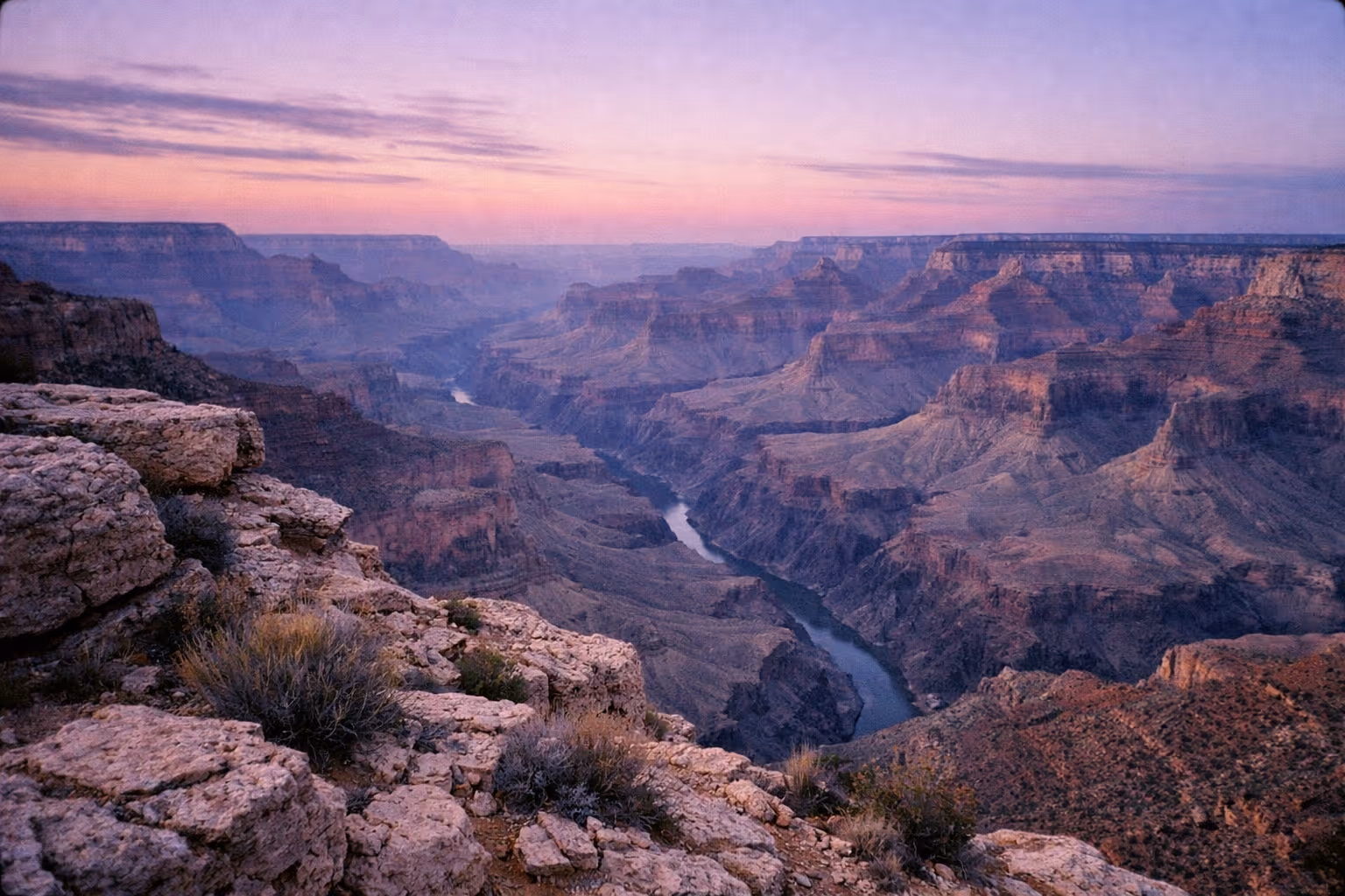 View of the Grand Canyon's layered cliffs and the Colorado River at sunset.
