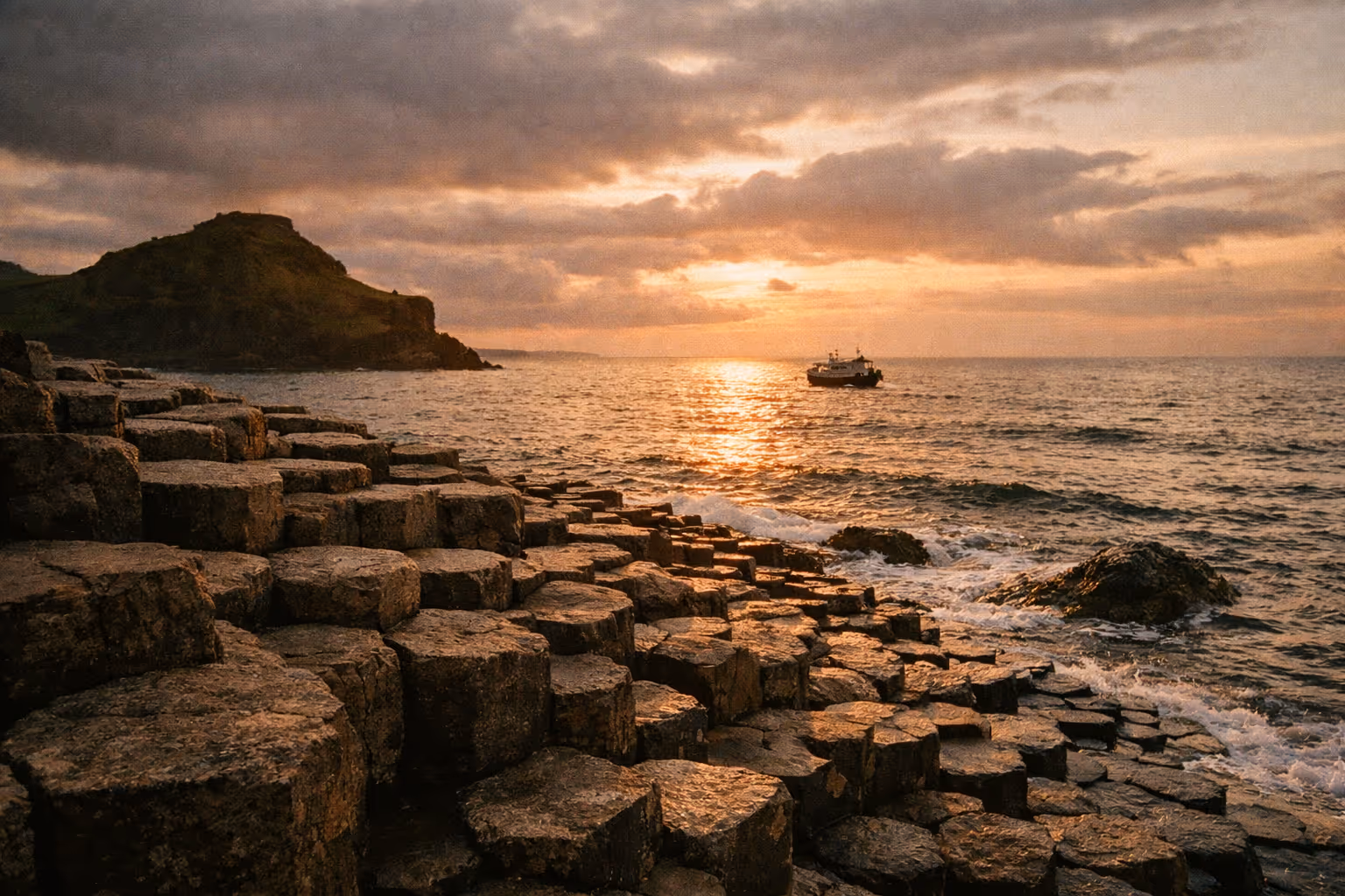 Basalt columns of the Giant's Causeway at the coast with a boat on the sea during sunset.