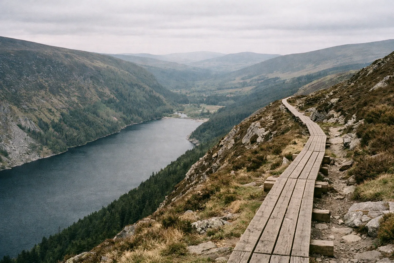 A wooden boardwalk follows the hillside above the Upper Lake in a wooded valley.