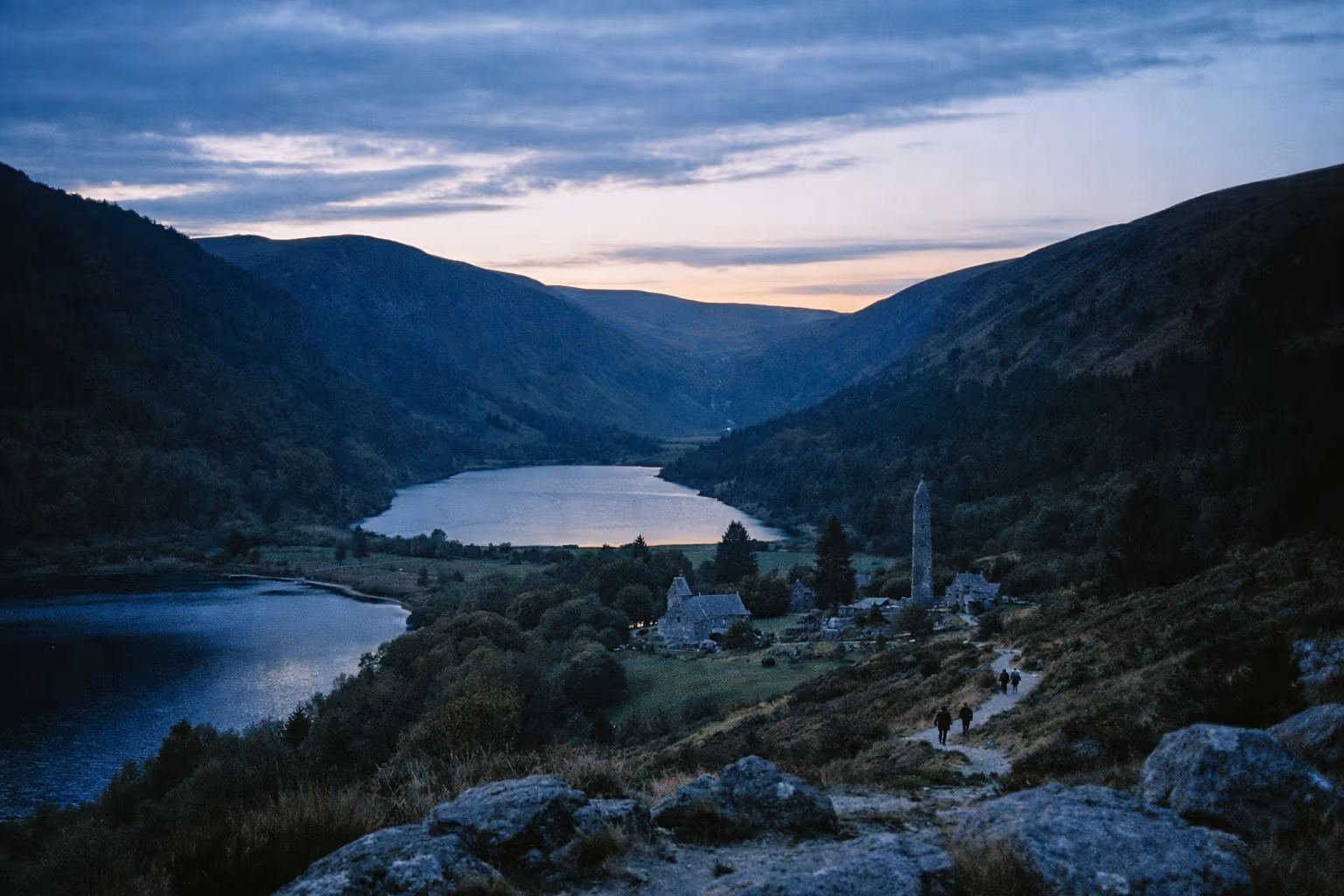 Glendalough monastic ruins and round tower beside lakes and mountains at dusk in the Wicklow Mountains.