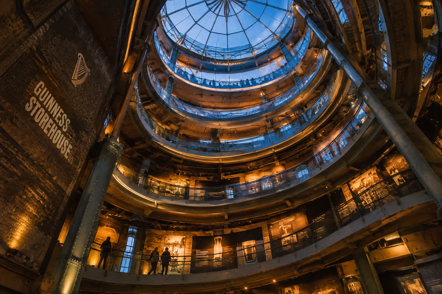 The Guinness Storehouse atrium rises beneath a glass roof, with curved visitor galleries around its brick interior.
