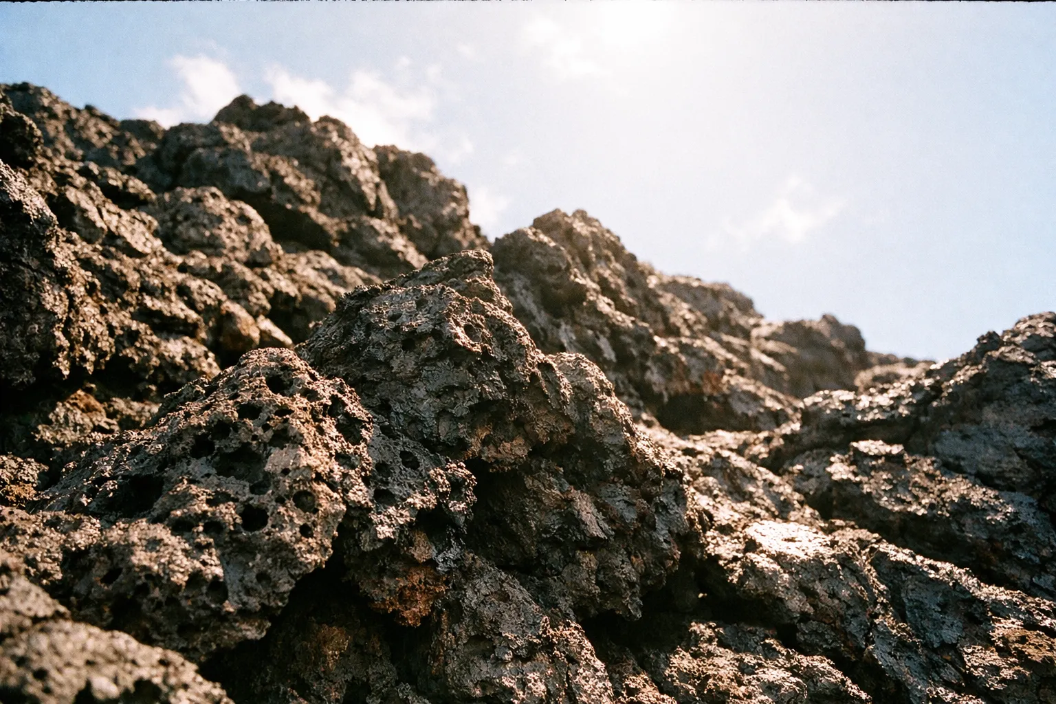 Jagged volcanic rocks under bright sunlight against a blue sky.