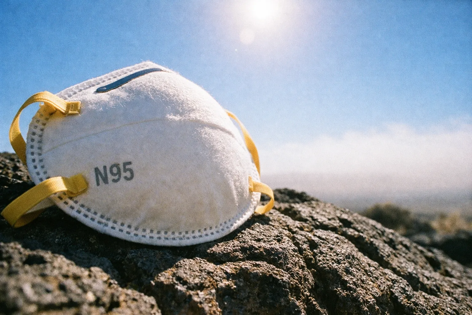 An N95 mask rests on volcanic rocks under a clear sky.