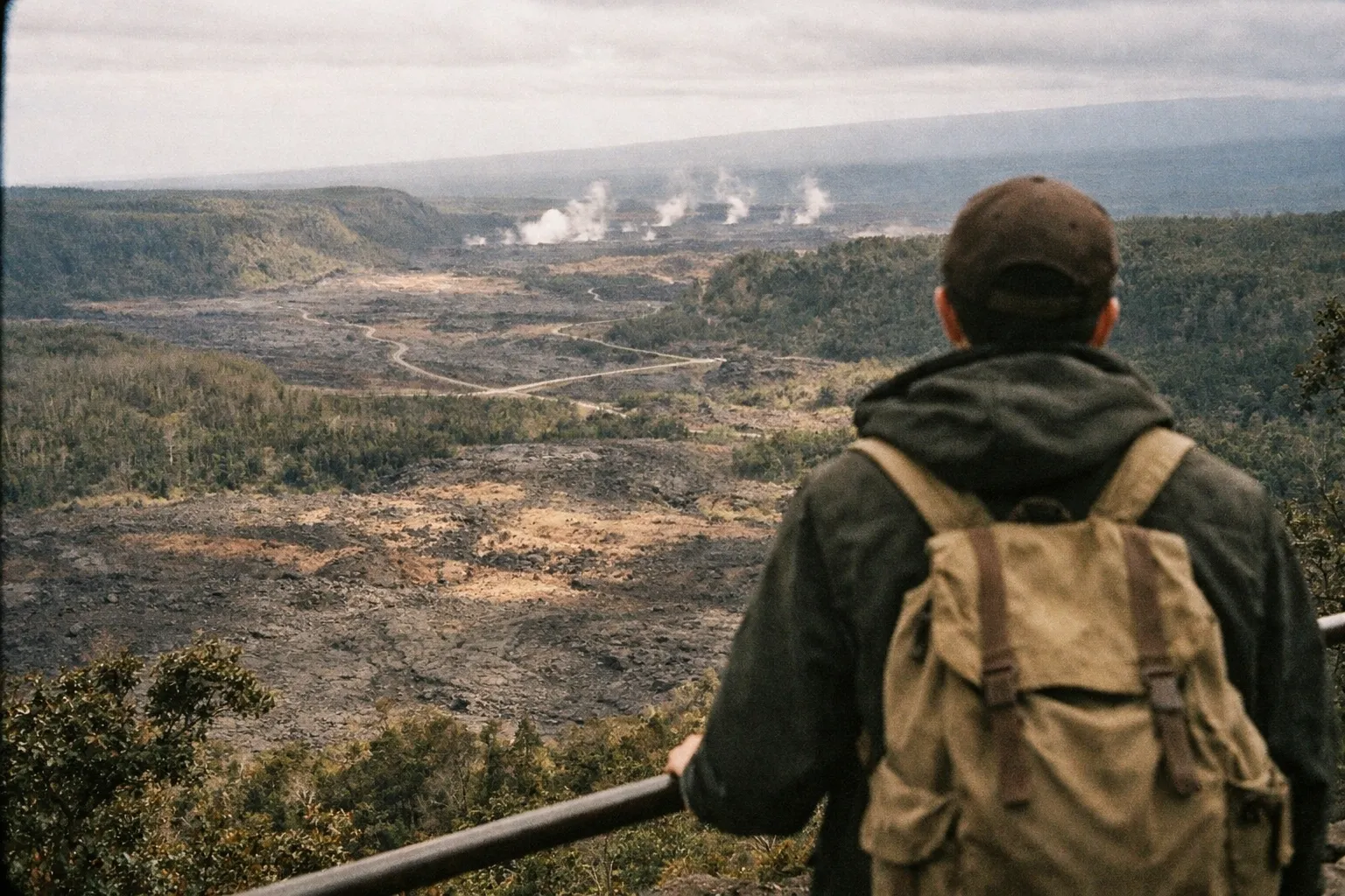 Person with a backpack looks over the volcanic landscape and steaming vents of Hawaii Volcanoes National Park.