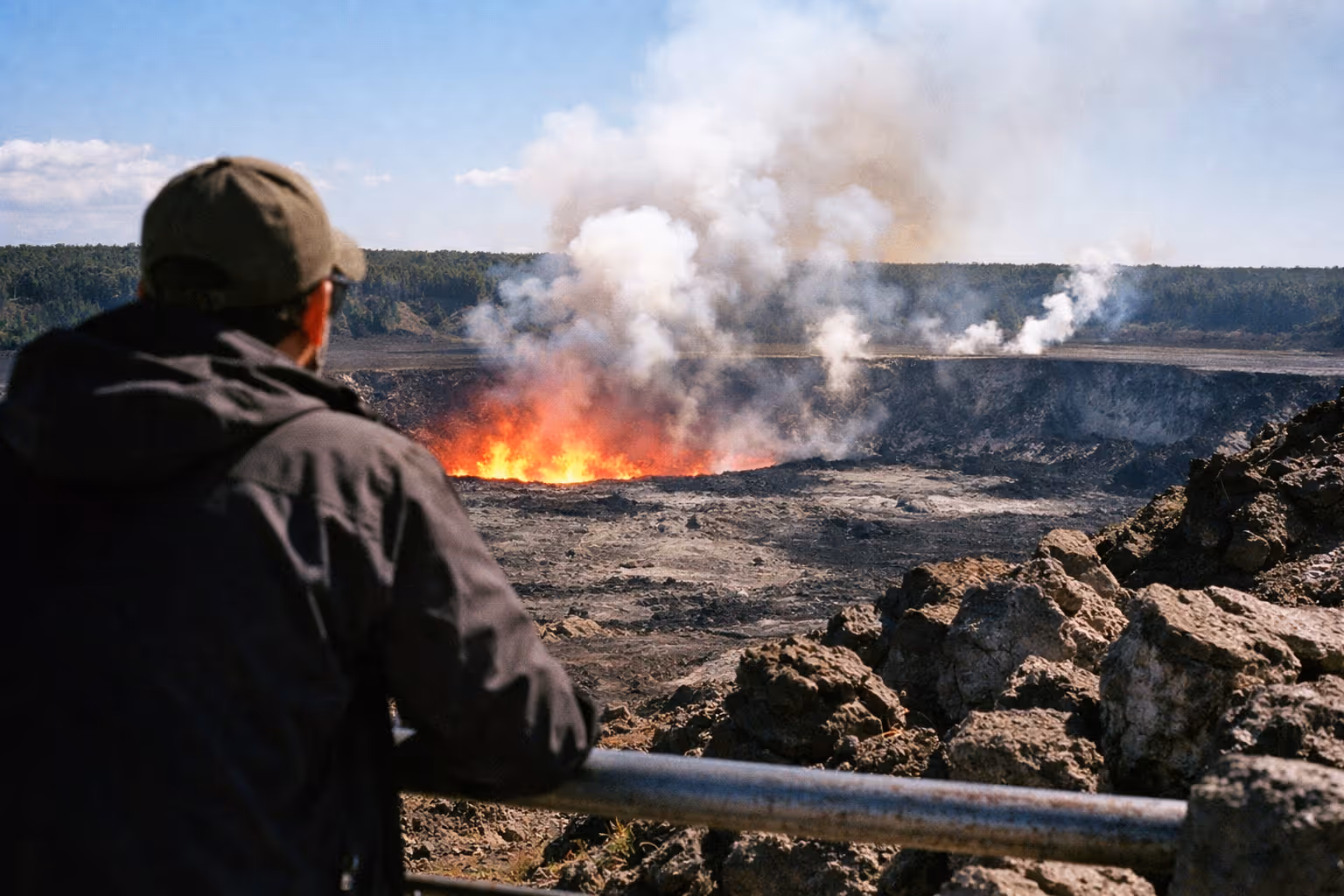 A person observes the Halema'uma'u crater with visible lava and smoke at Hawaii Volcanoes National Park.