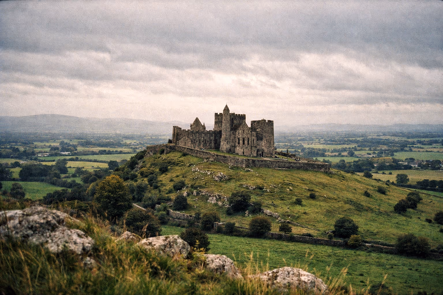 The Rock of Cashel sits atop a green hill surrounded by fields in the Irish countryside.
