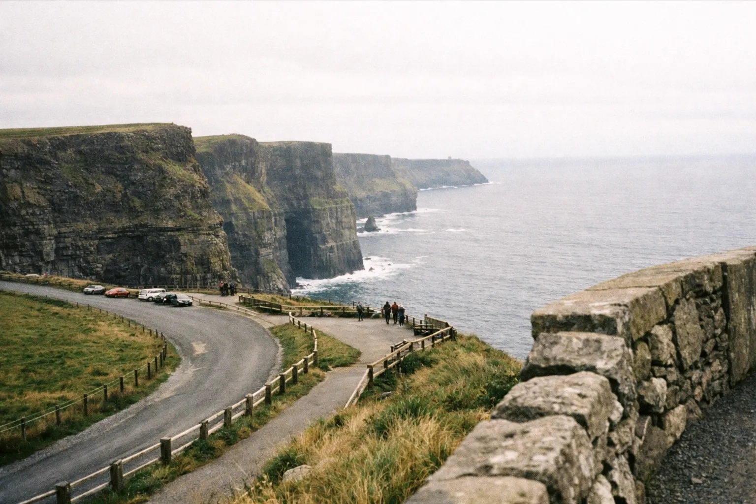Visitors walk near parked cars along the Cliffs of Moher overlooking the Atlantic Ocean in Ireland.
