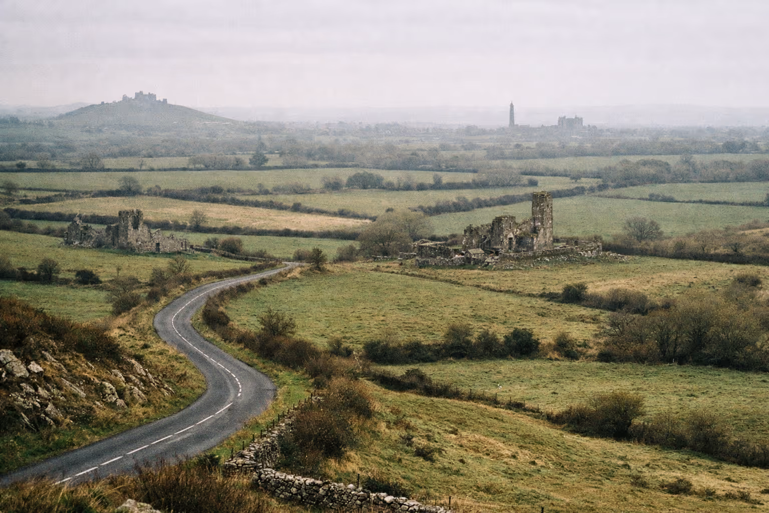 A winding country road passes by Hore Abbey ruins with the Rock of Cashel in the background, set in green Irish countryside.