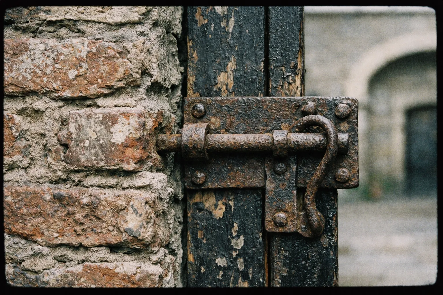 A rusty metal bolt secures an old wooden door set in a weathered brick wall at Kilmainham Gaol.