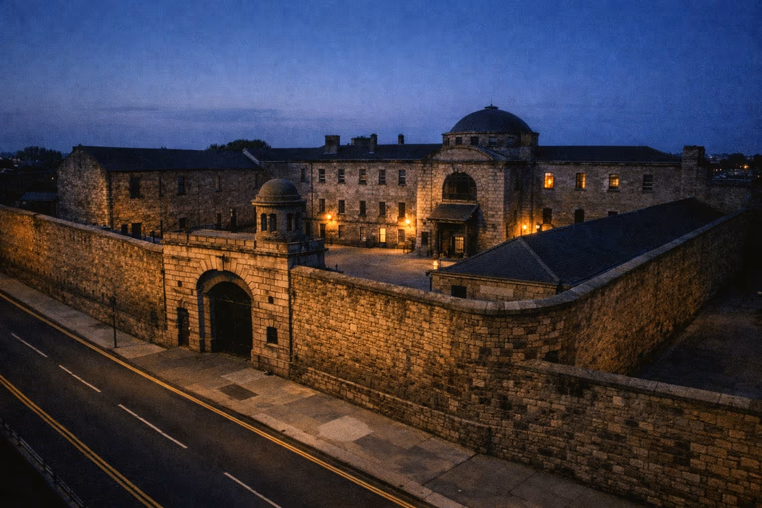 Kilmainham Gaol's stone exterior and main entrance illuminated at dusk in Dublin, Ireland.