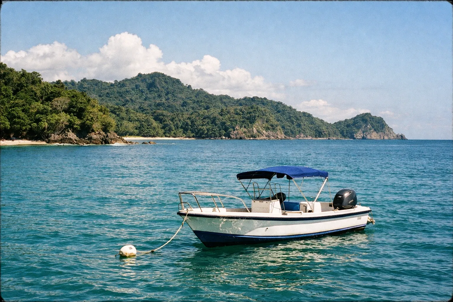 A small motorboat floats near the shore of a lush, forested coastline at Manuel Antonio National Park.