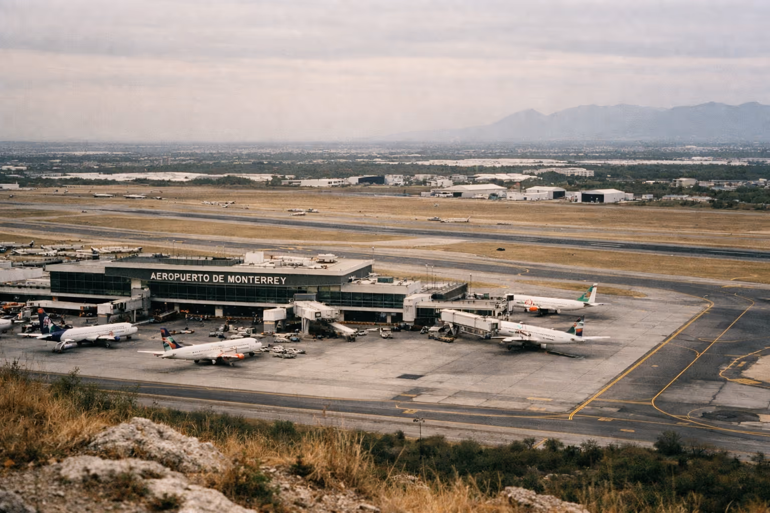 A view of Aeropuerto de Monterrey with several airplanes parked at the terminal and runways in the background.