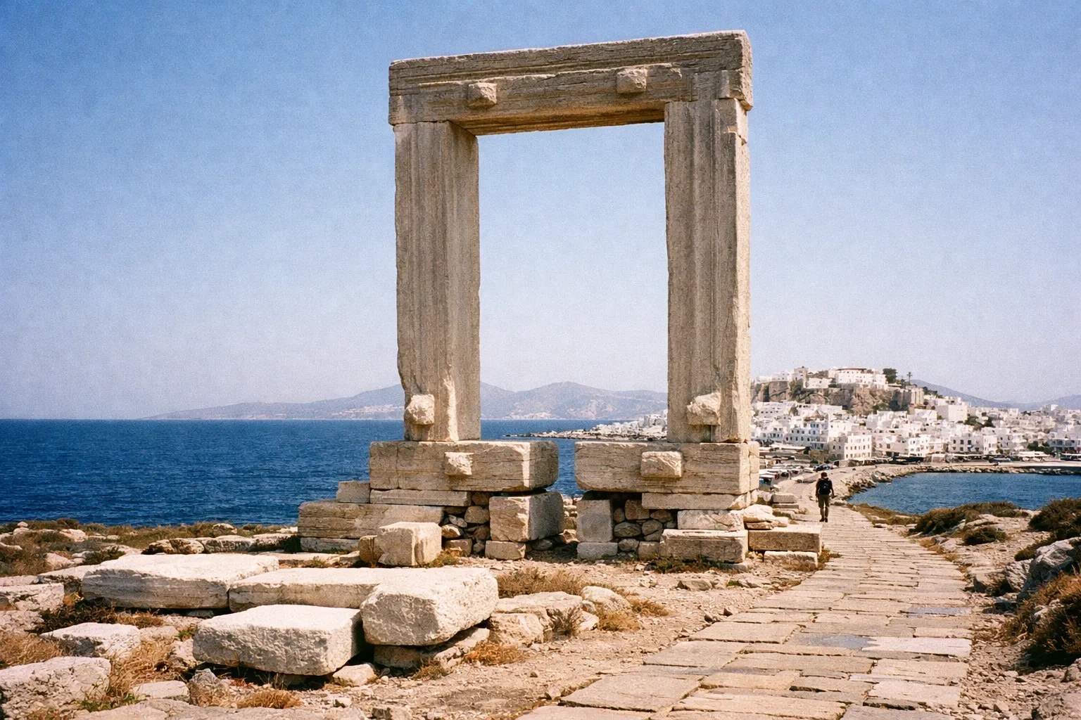 The Portara stone gateway stands by the sea with Naxos town and hills in the background.