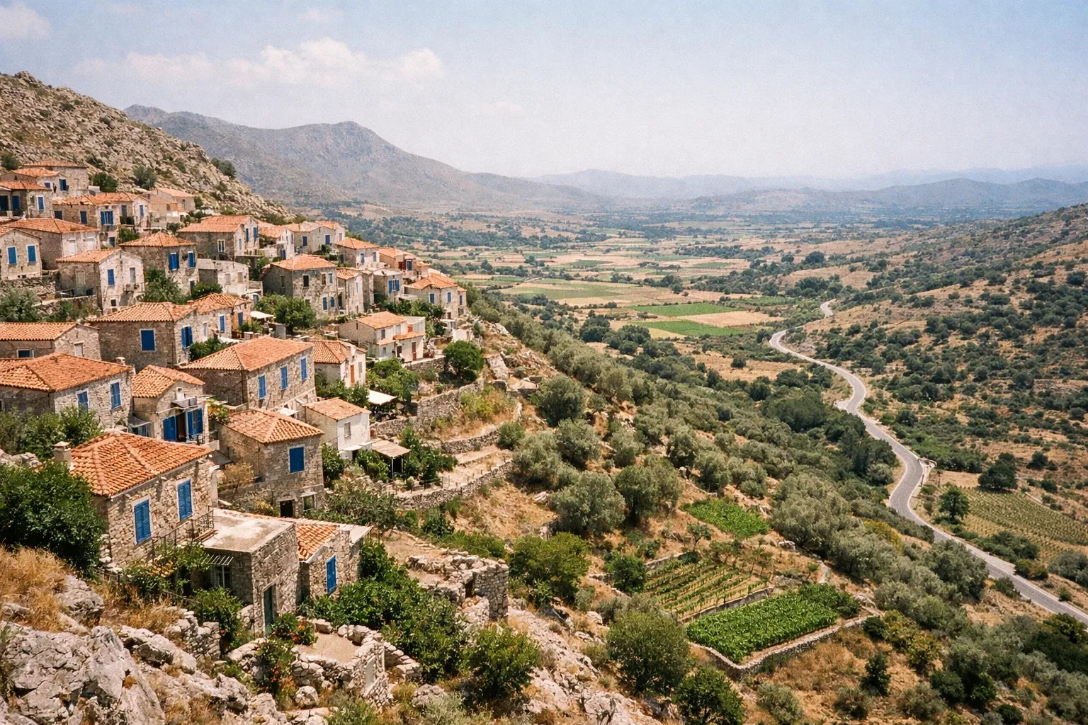 Stone houses with red tile roofs and blue shutters line a hillside in a mountain village overlooking farmland on Naxos.